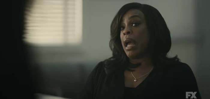 Niecy Nash in a dramatic scene speaking to someone off camera, likely from TV series on FX. She is wearing a dark outfit with a necklace