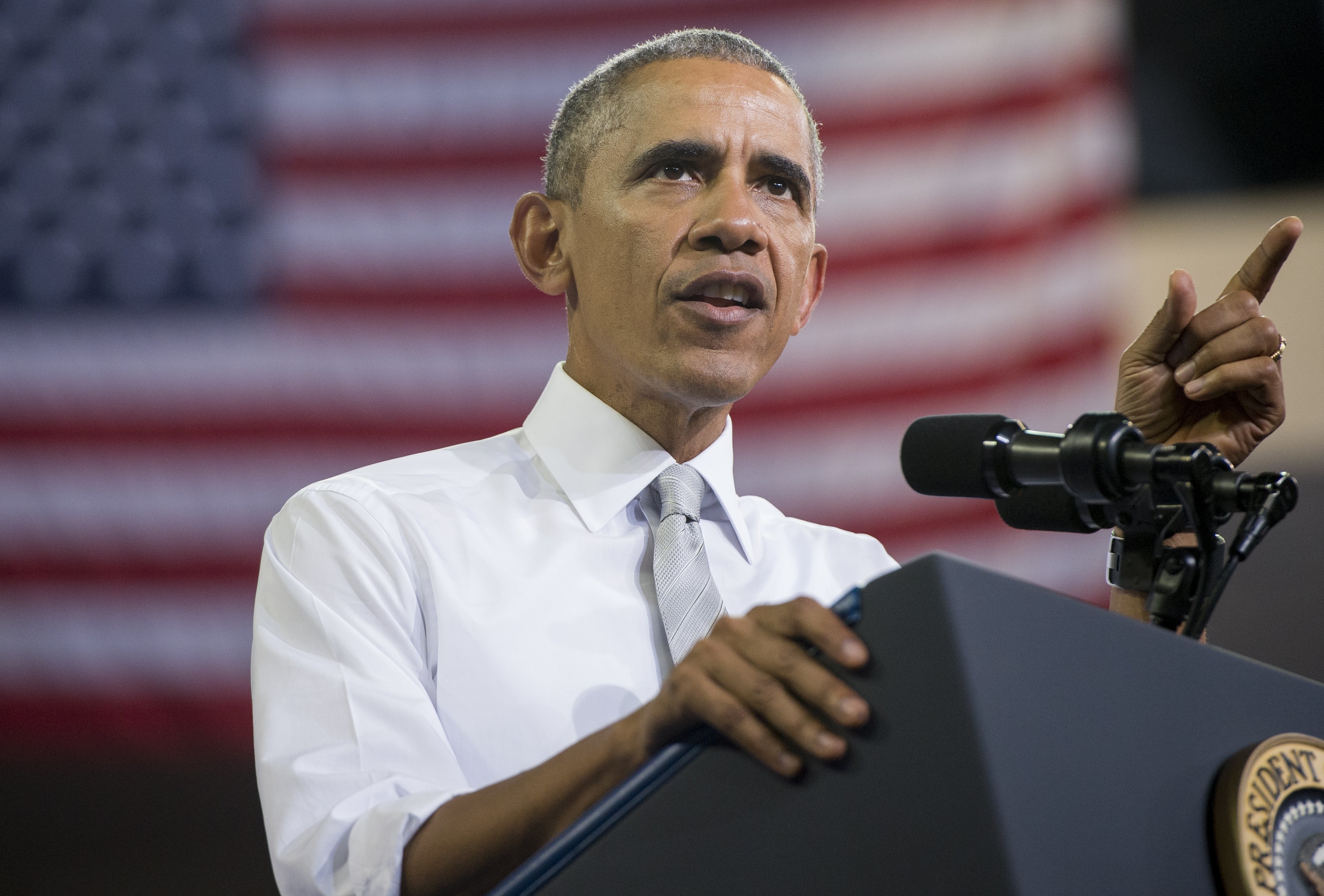 Barack Obama at a podium, speaking and pointing into the distance with an American flag in the background