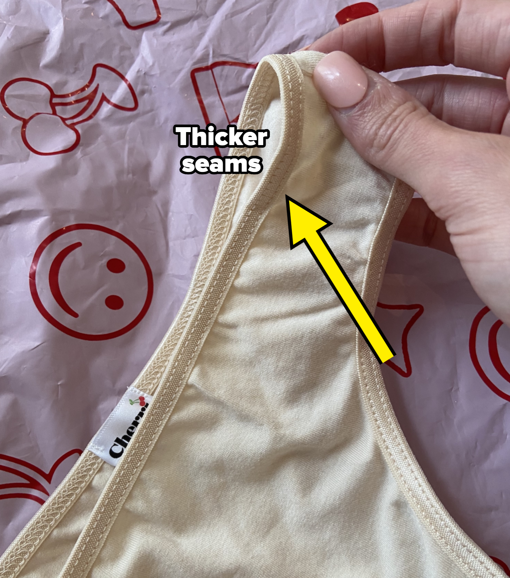 A hand holding a light-colored fabric with a label that says "Chan"; background features red outlined playful shapes, including a smiling face