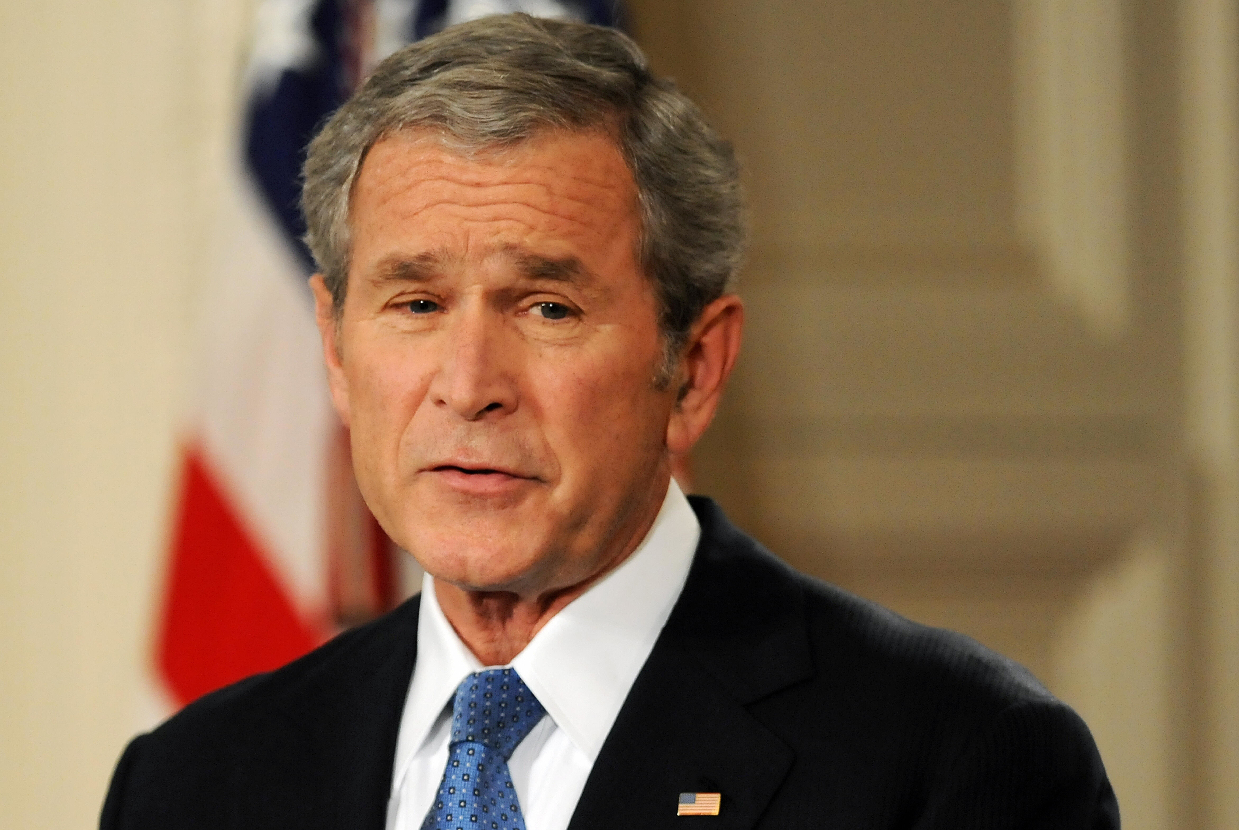 George W. Bush in a suit with an American flag pin, delivering a speech