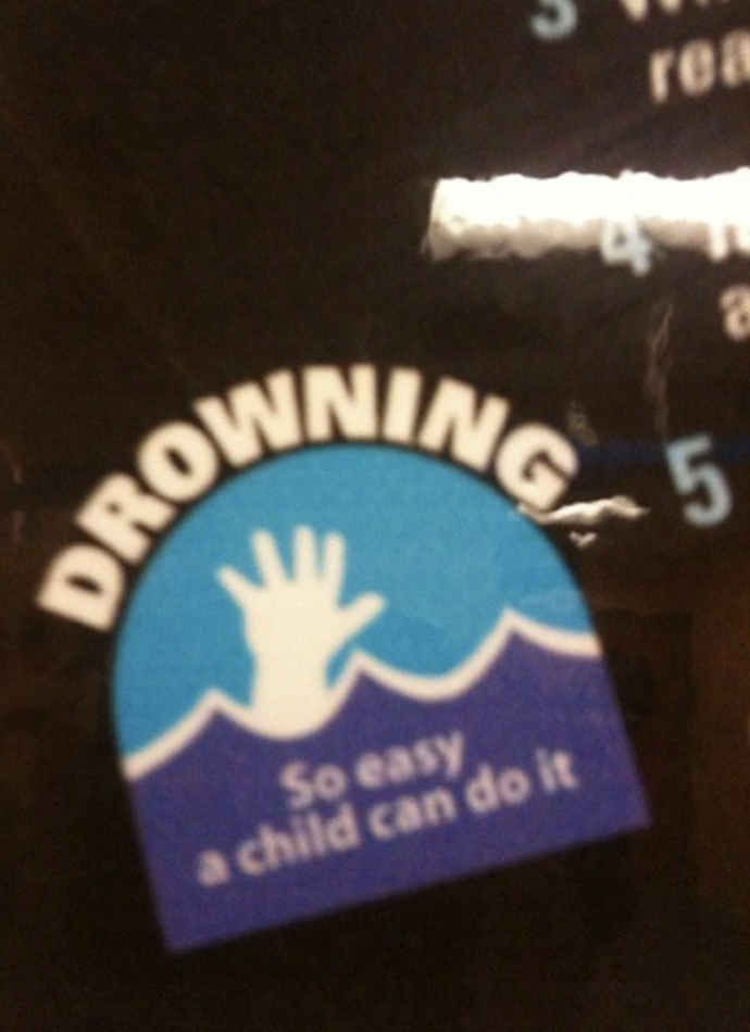 A sign with the text "Drowning. So easy a child can do it" and an image of a hand reaching up through the water waves