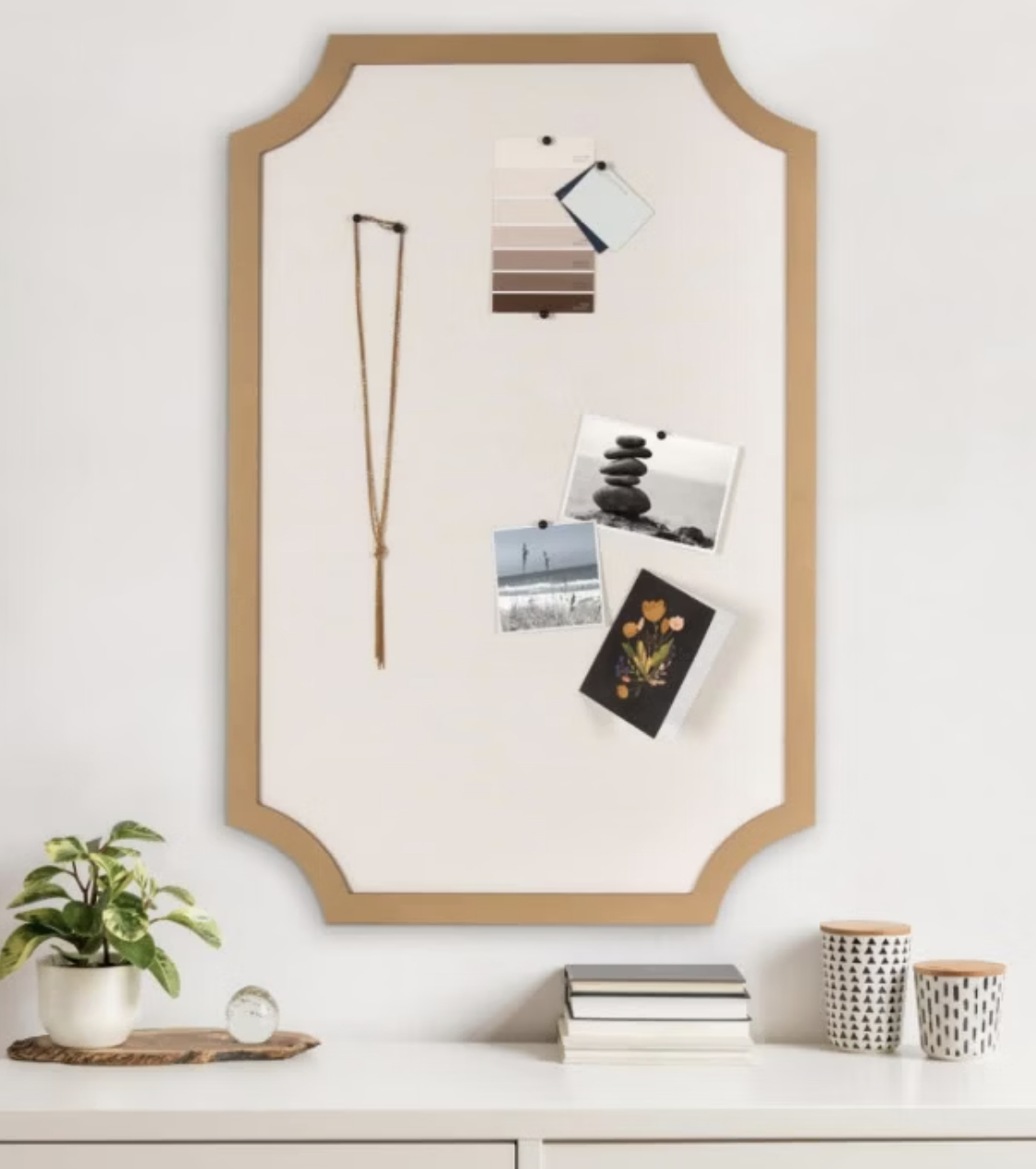 Office space framed board featuring a hanging necklace, color palettes, decorative photos, with a plant, clock, books, and two mugs on a surface below