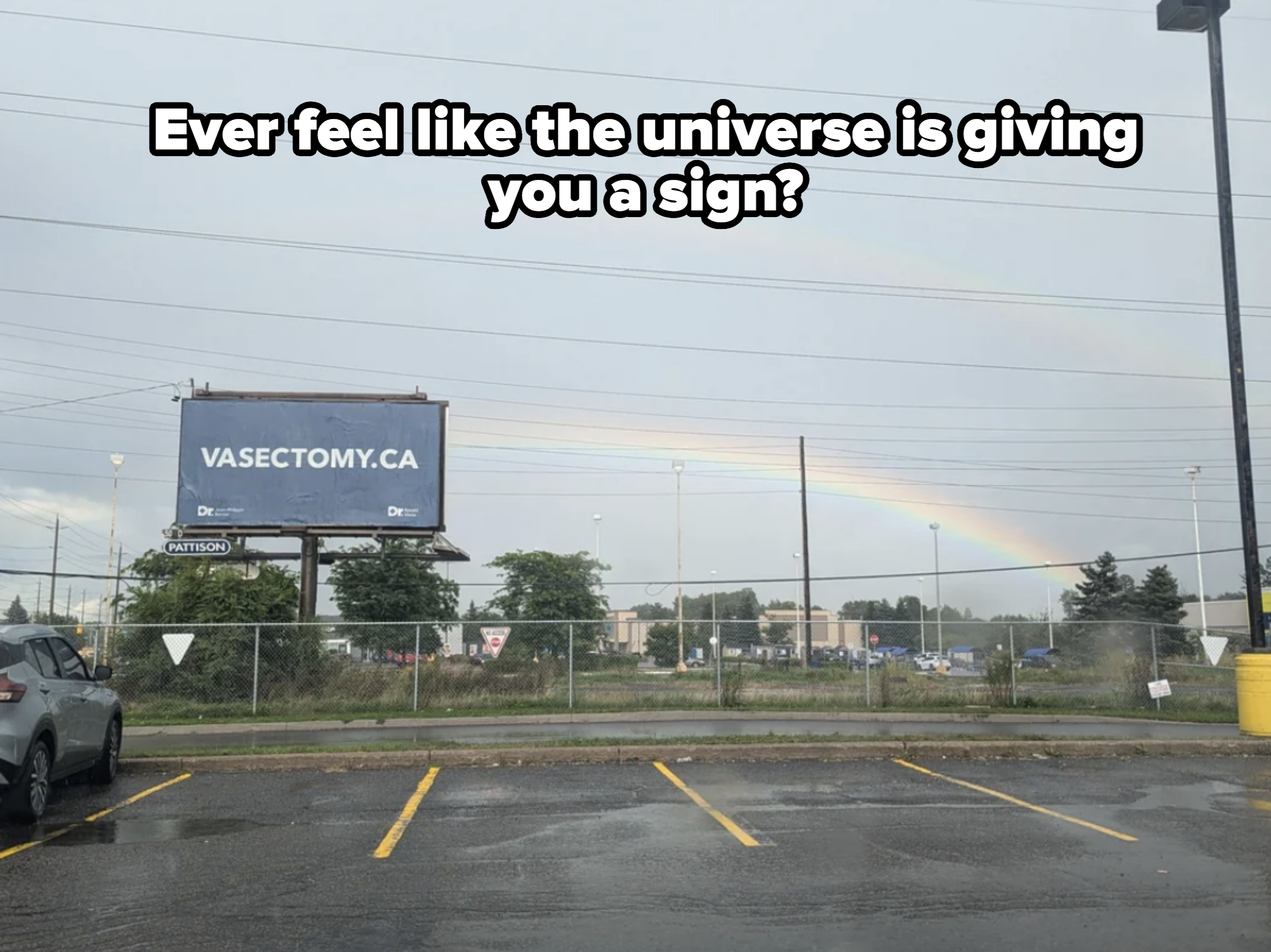 A billboard in a parking lot promotes Vasectomy.ca, with a double rainbow visible in the cloudy sky above