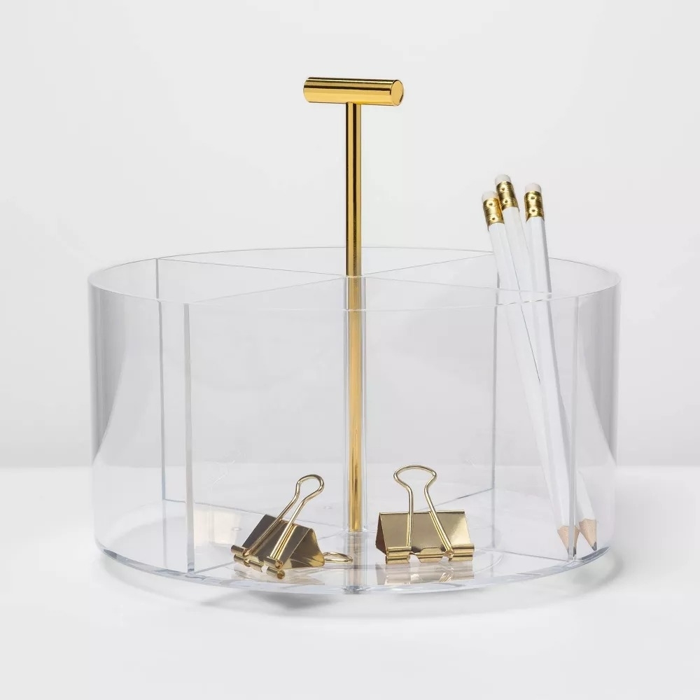 Clear acrylic desk organizer with a gold handle, holding gold binder clips and white pencils