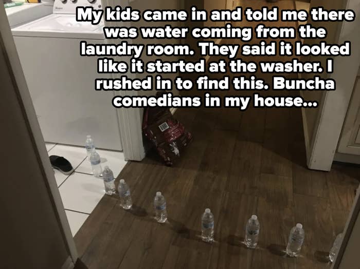 Seven bottled waters are lined up in a hallway near a laundry area with a washer in view.