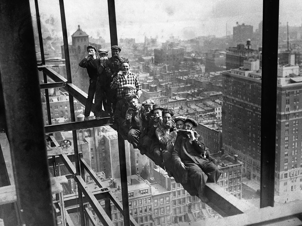 Eleven construction workers sit on a steel beam high above New York City, eating lunch during the construction of Rockefeller Center in 1932