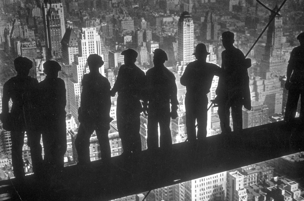 Construction workers sitting on a steel beam high above New York City in the 1930s, with the cityscape in the background