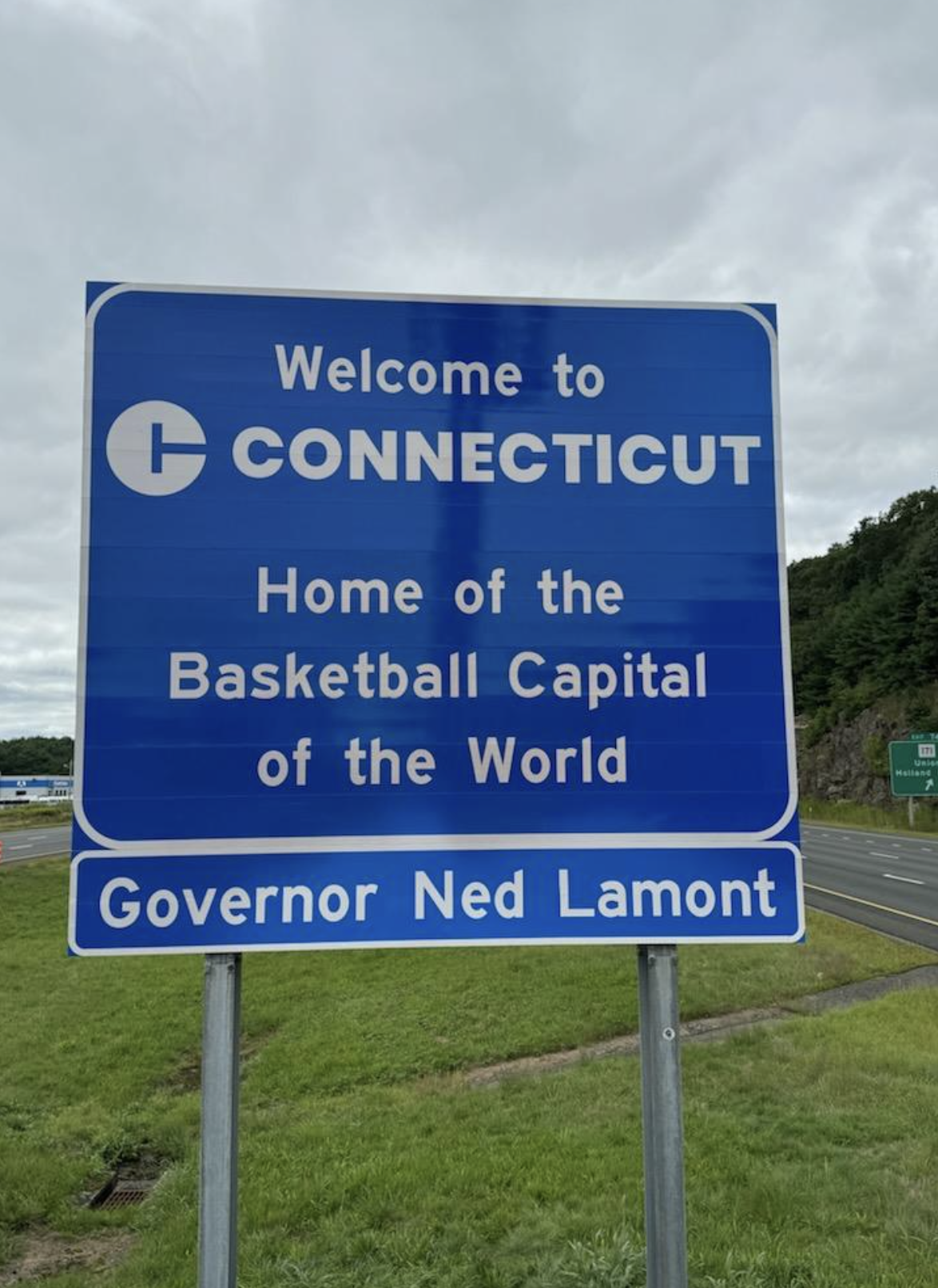 A blue road sign reads, &quot;Welcome to Connecticut. Home of the Basketball Capital of the World. Governor Ned Lamont.&quot;