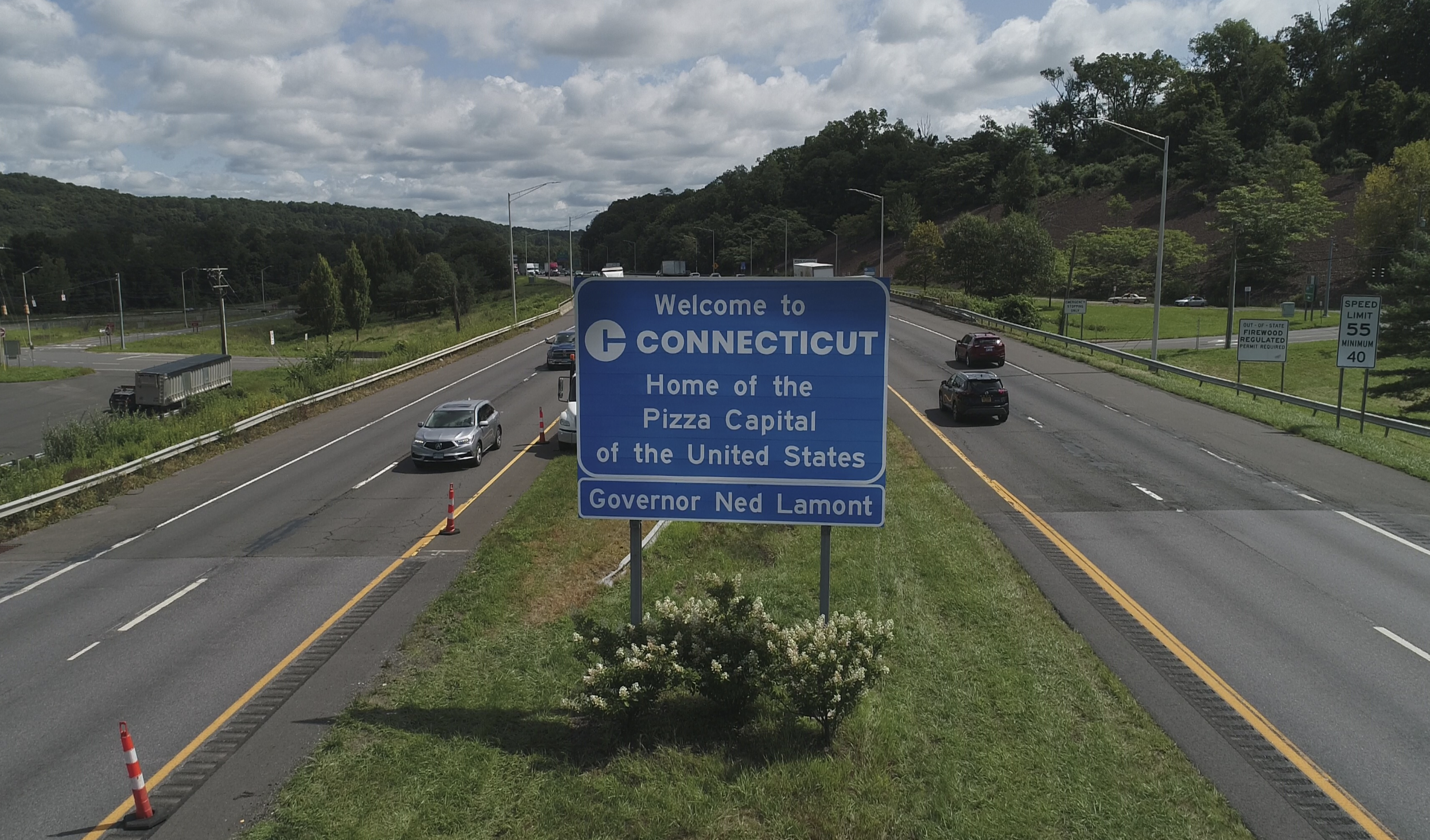 &quot;Welcome to Connecticut&quot; highway sign, reading &quot;Home of the Pizza Capital of the United States. Governor Ned Lamont&quot; with cars on the road in the background