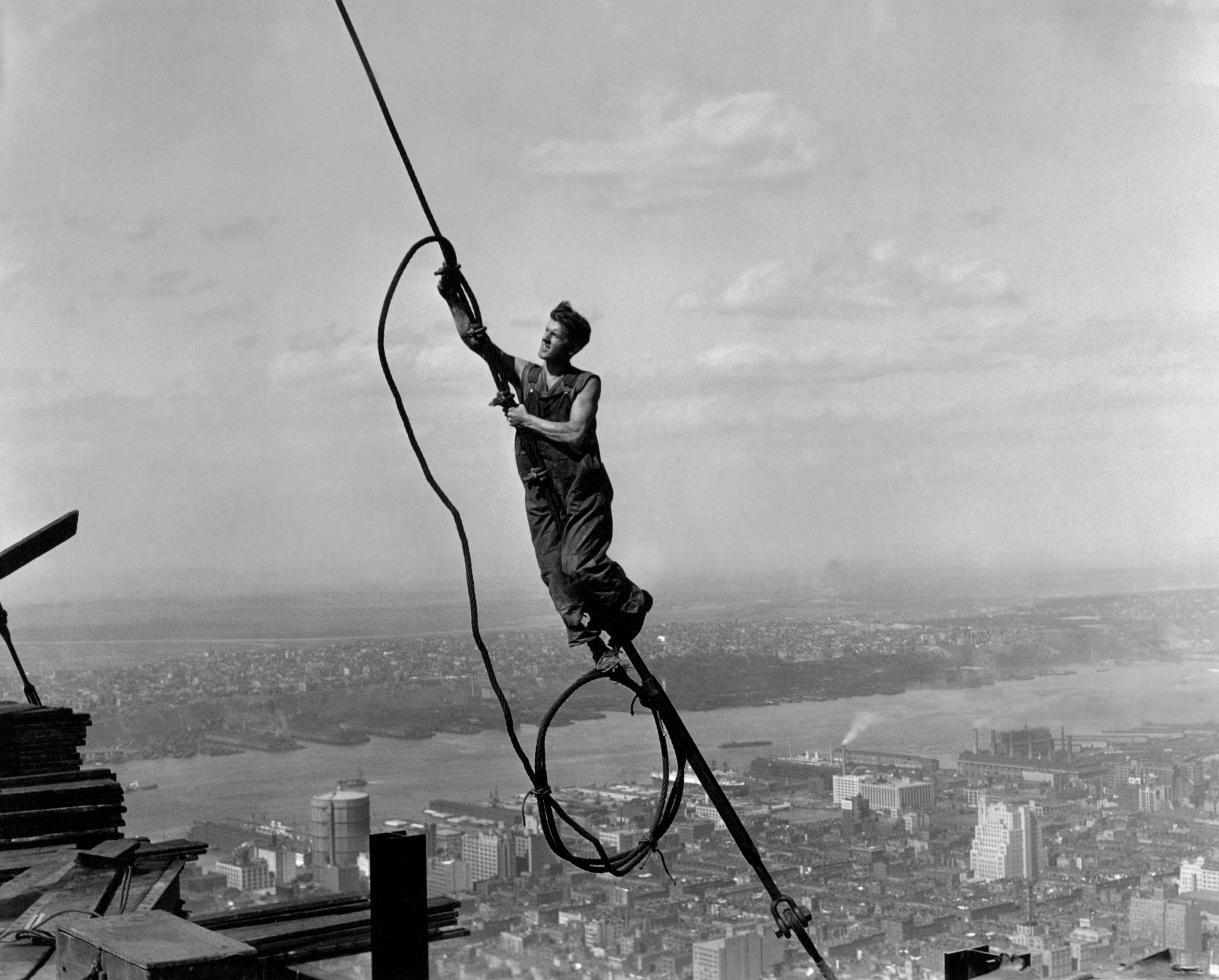 Man balancing on a steel girder high above New York City during the construction of the RCA Building, 1932. The cityscape and river are visible below
