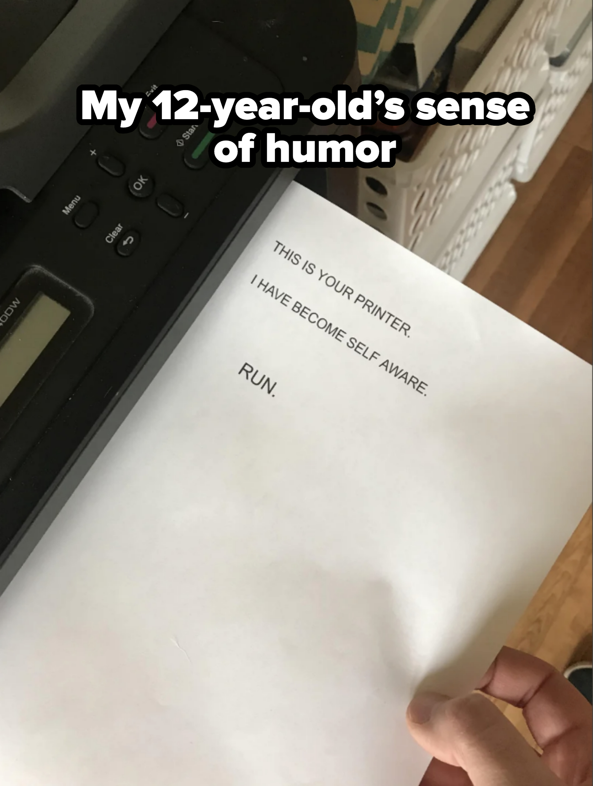 A piece of paper exits a printer with printed text stating: "THIS IS YOUR PRINTER. I HAVE BECOME SELF AWARE. RUN"