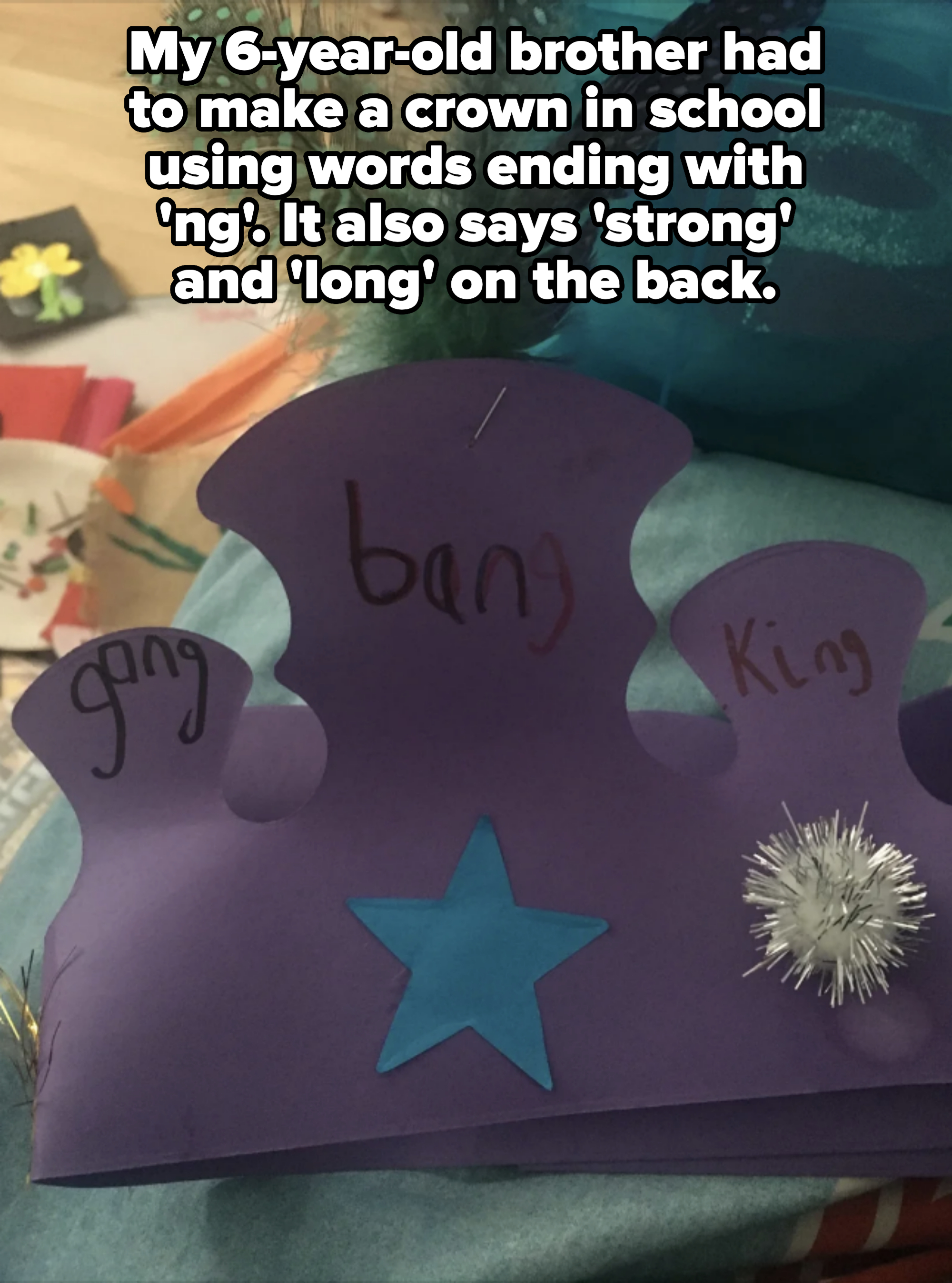 Handmade purple paper crown with a blue star and pom-pom decorations. Feathers are attached to the top. The words "gang," "bang," and "King" are written on it
