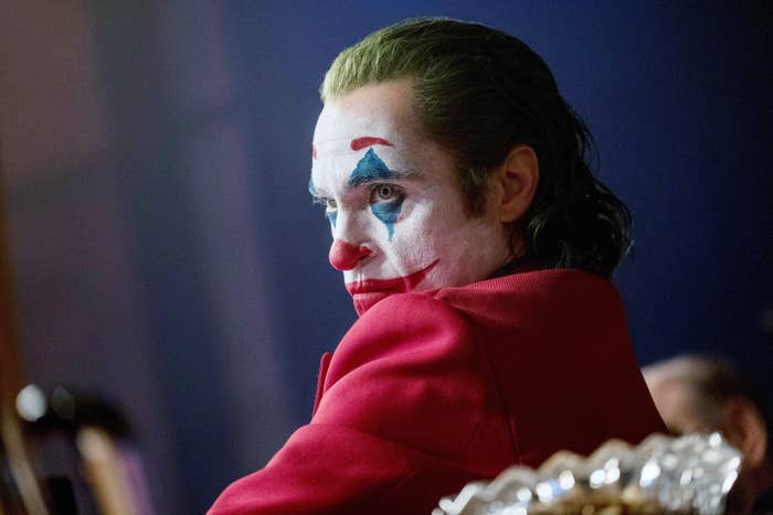 Joaquin Phoenix as the Joker in a still from the movie &quot;Joker,&quot; wearing white face paint with blue and red accents and a red jacket