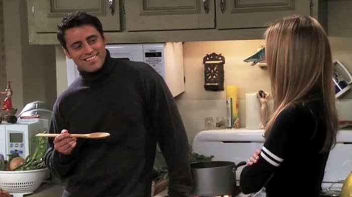 Matt LeBlanc and Jennifer Aniston in a kitchen scene from Friends, with Matt holding a wooden spoon and smiling at Jennifer