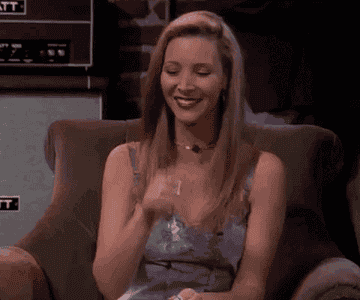 Lisa Kudrow as Phoebe Buffay in Friends sits on a couch and waves her hand near her ear, pretending she can't hear