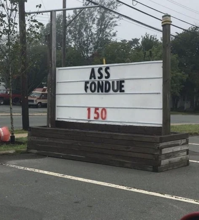 Storefront sign with text "ASS FONDUE" and "150." Nearby are trees, parked vehicles, and power lines in the background