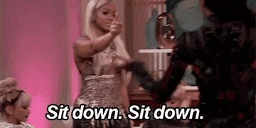 Two women in a dramatic moment on a talk show, one standing and pointing, saying &quot;Sit down. Sit down.&quot; The other person is partially turned away