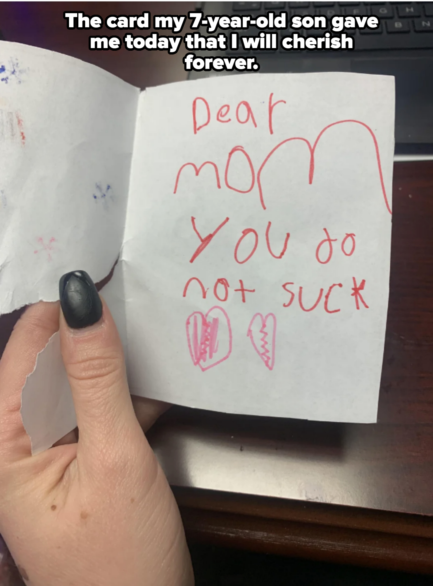 A hand holding a handwritten card saying, "Dear Mom, You do not suck," with two drawn hearts