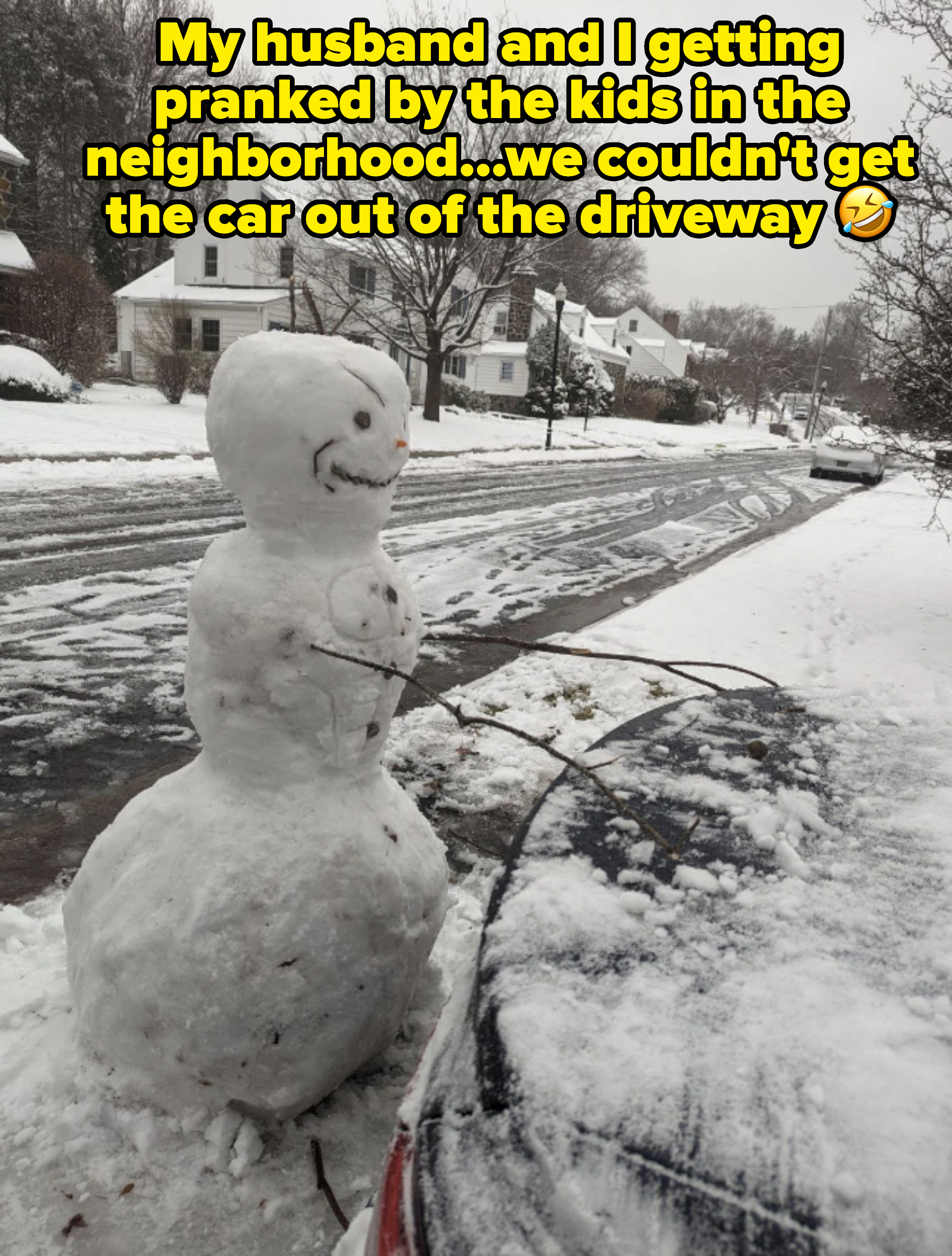 A snowman stands next to a snow-covered car on a residential street, blocking the car in