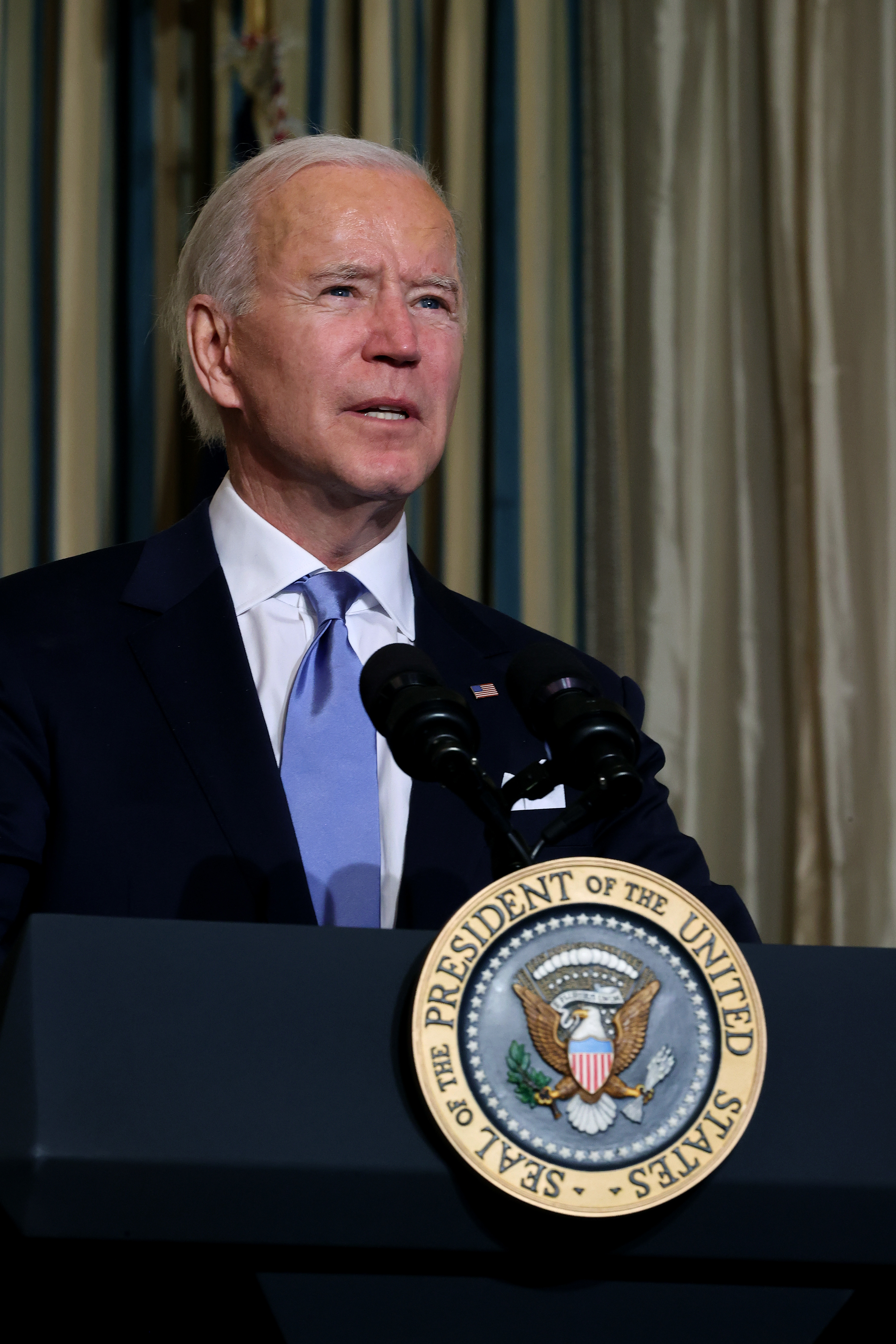Joe Biden stands at a podium with the Seal of the President of the United States, speaking into microphones