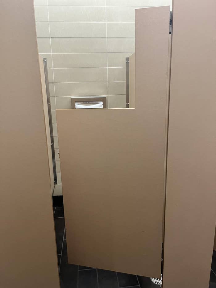 A public restroom stall with a poorly designed door revealing a large gap, compromising privacy