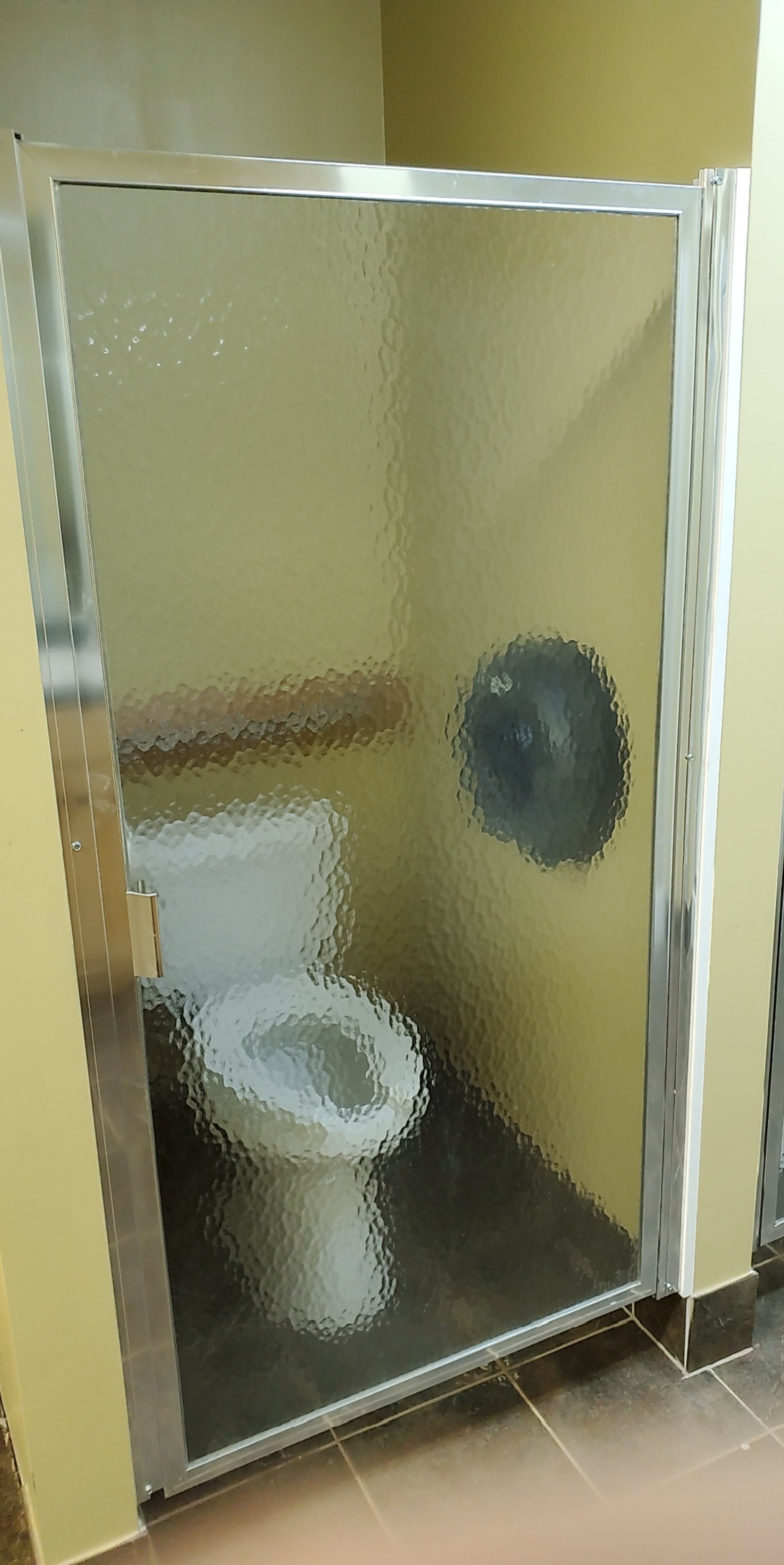 Restroom with a stall having a frosted glass door, inside is a toilet and a toilet paper dispenser