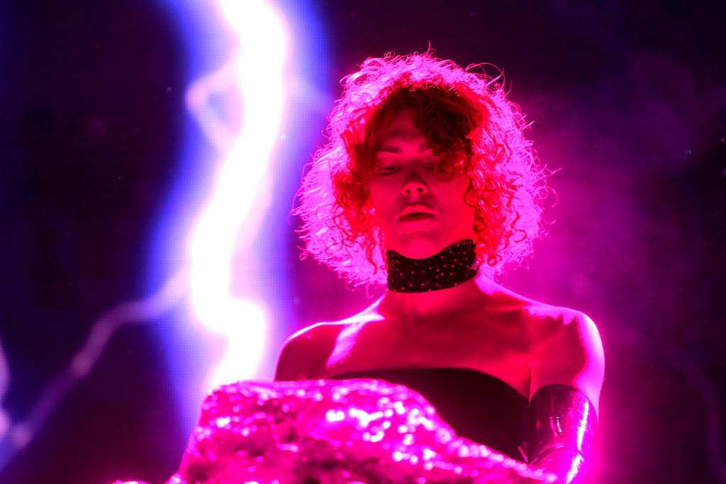 Sophie on stage, wearing a strapless top and a choker, under dramatic lighting with a bright streak of light behind her