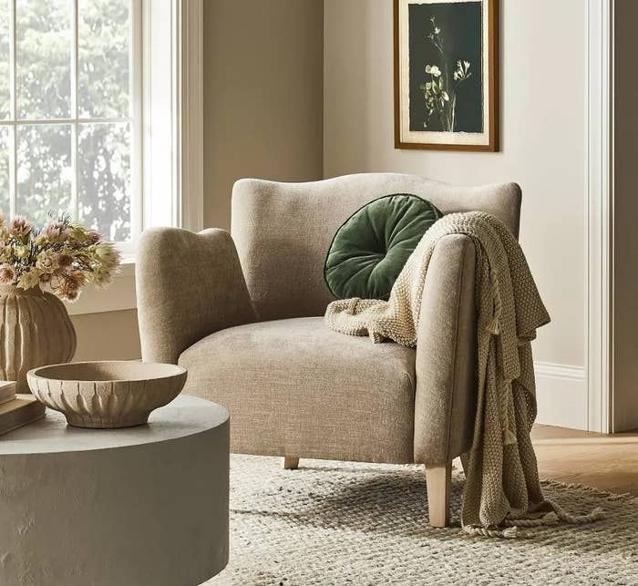 Modern living room with a cozy armchair, a green pillow, a knitted throw, and art on the wall
