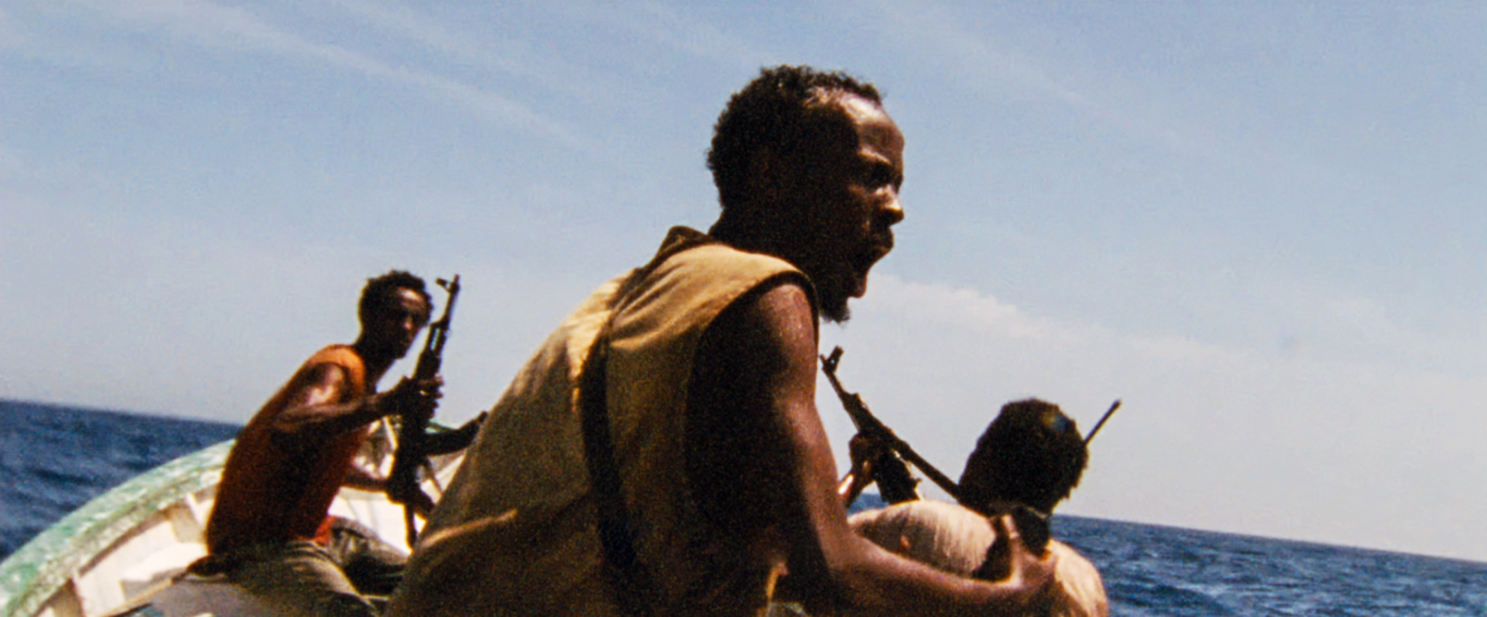 Three men on a boat, armed with rifles. One man is shouting, possibly giving instructions, while the other two are looking in different directions