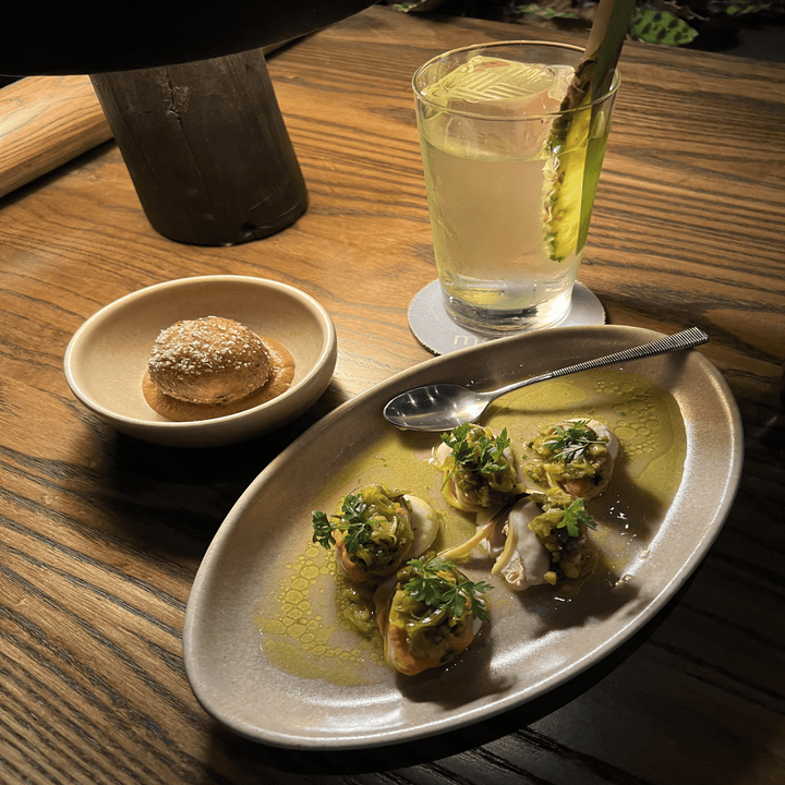 solo trip to japan itinerary Plate of oysters with garnishes, a bread roll with butter, and a cocktail on a wooden table