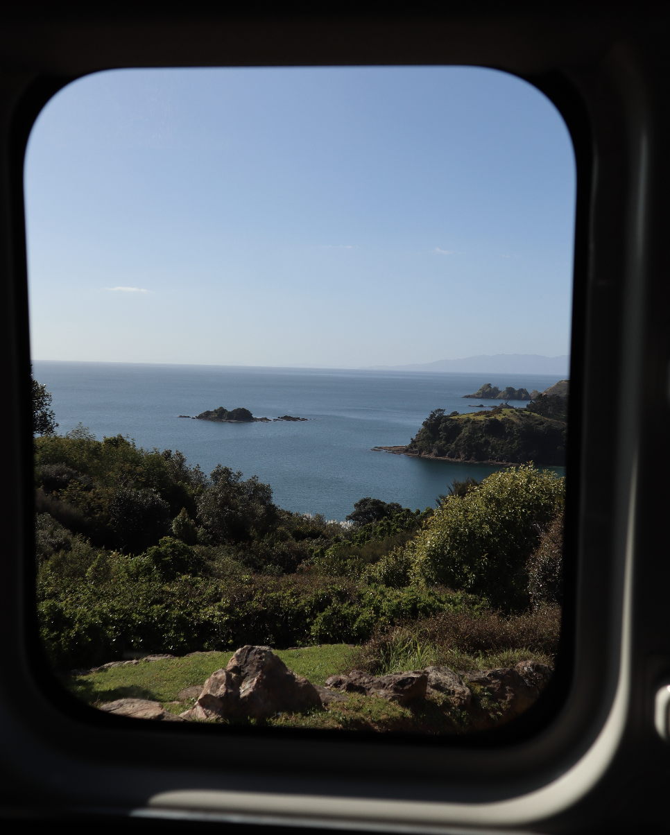 View of a serene coastal landscape with lush greenery, rocky shoreline, and distant islands as seen through a window