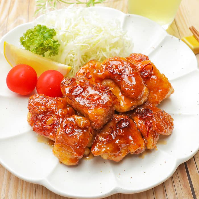 白い皿に盛られたチキン、添え野菜にキャベツの千切り、トマト、レモンが添えられています。