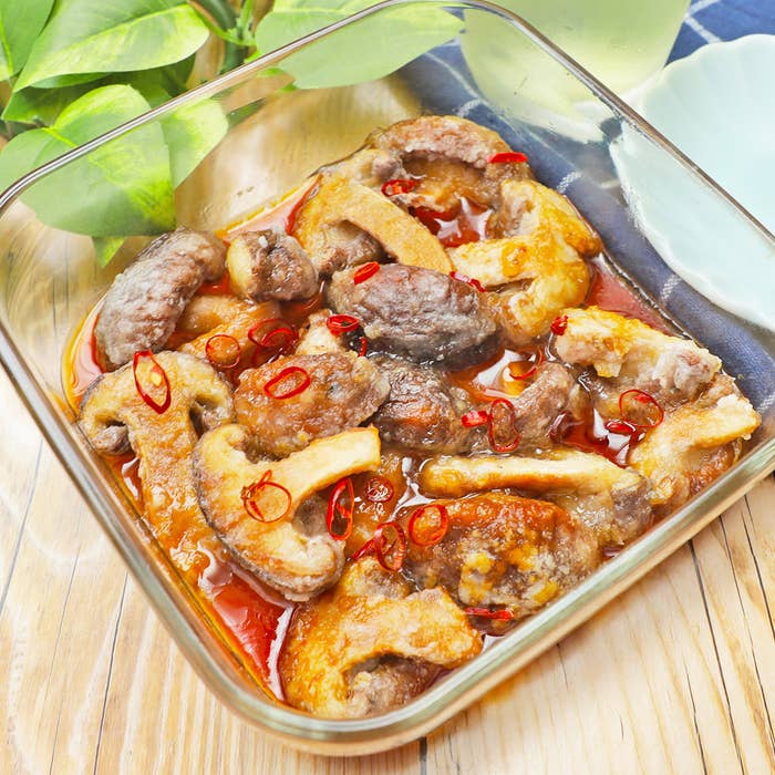 ガラスの器に盛られたキノコ。唐辛子のスライスがトッピングされている。背景にはグリーンの葉。