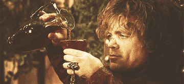 Peter Dinklage is pouring wine into a glass while looking focused
