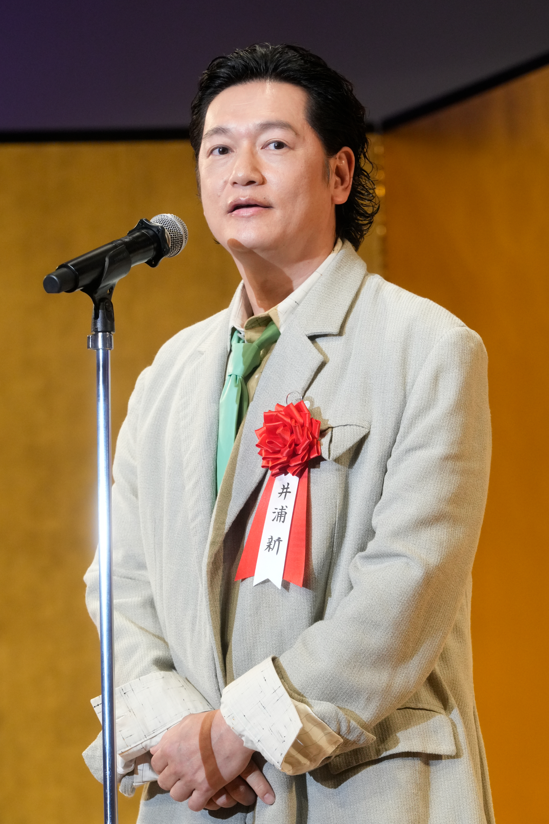 井浦新さんがスーツ姿でスピーチしている。