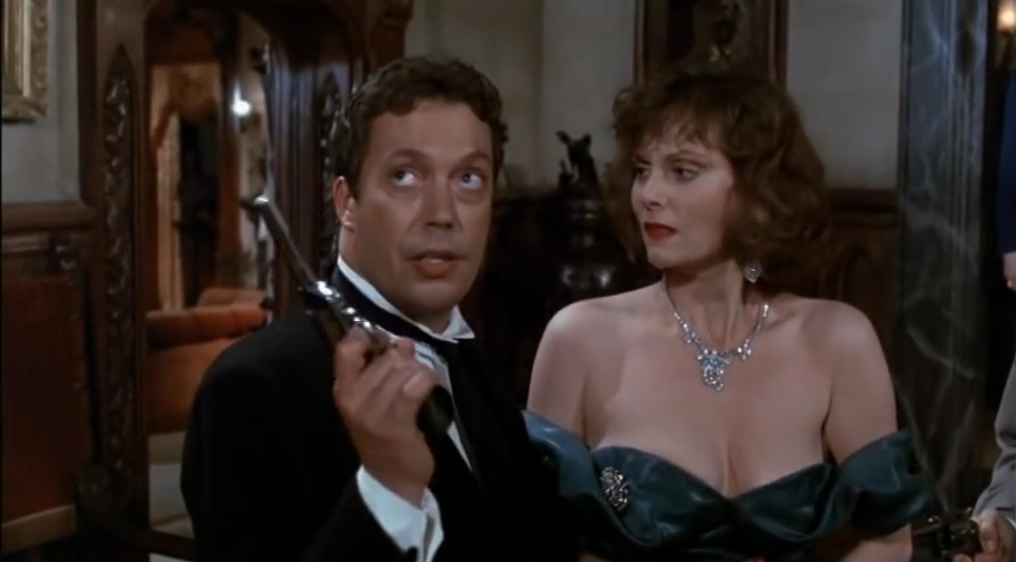 Michael McKean holds a revolver while Lesley Ann Warren, dressed in a glamorous strapless gown with a diamond necklace, looks at him