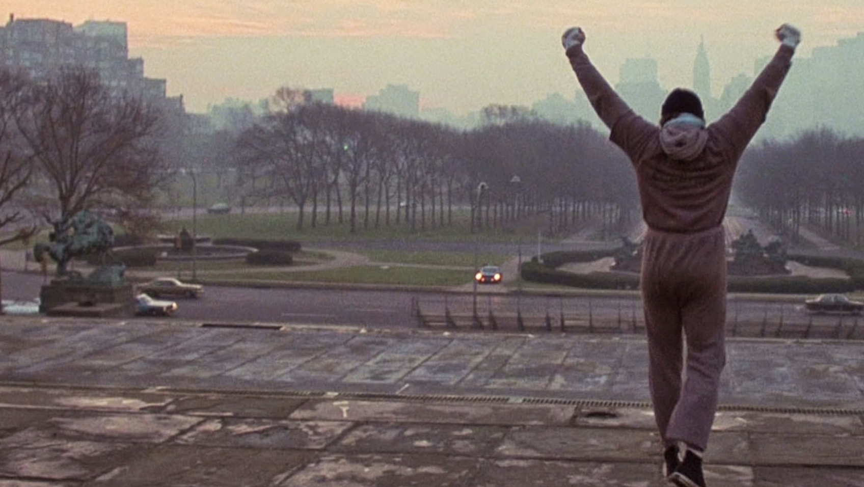 Sylvester Stallone as Rocky Balboa triumphantly raises his arms at the top of the Philadelphia Museum of Art steps at dawn in a famous training scene