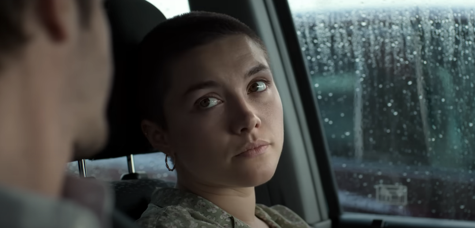 Florence Pugh gazes intently at a person in a rainy car scene for We Live in Time