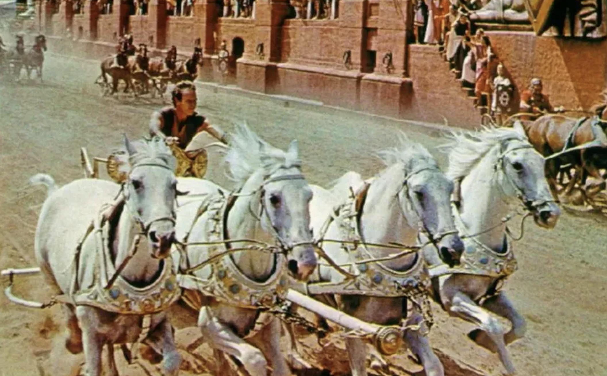 A scene from the movie "Ben-Hur" showing a chariot race with four white horses and a charioteer, played by Charlton Heston, racing in an arena