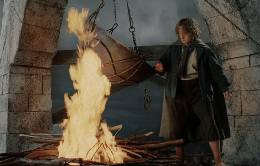 A character from the Lord of the Rings series, dressed in a cloak and looking determined, stands next to a large fire, about to drop an object into it
