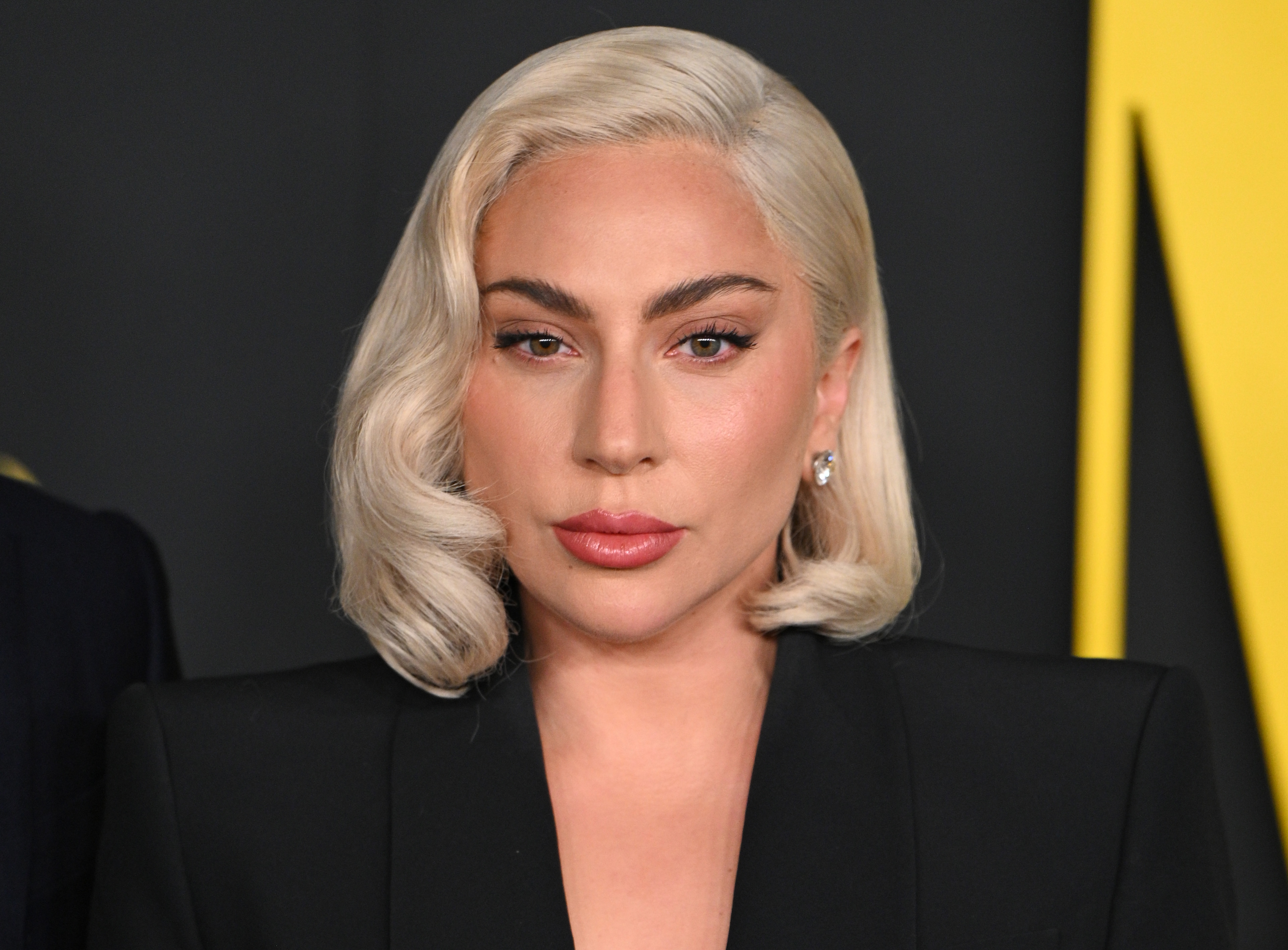 Lady Gaga with platinum blonde hair and wide-shoulder black blazer poses for a photograph