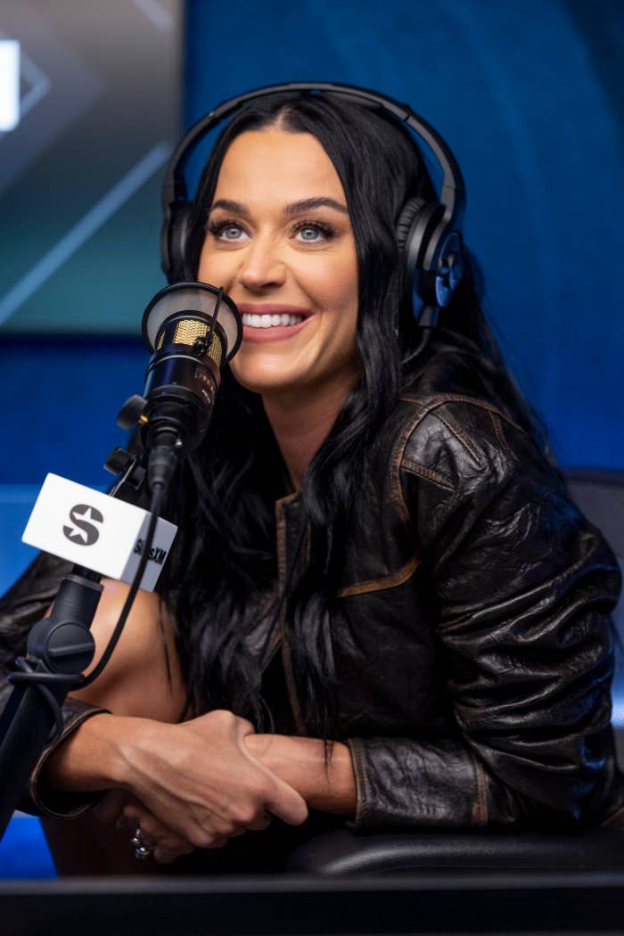 Katy Perry smiles while wearing headphones and a leather jacket during a radio interview