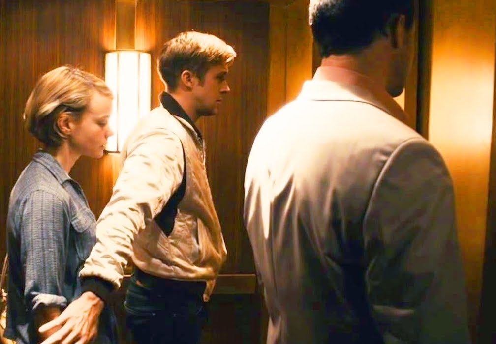 Ryan Gosling extends his arm to protect Carey Mulligan while standing in an elevator with another man in a still from the movie "Drive."