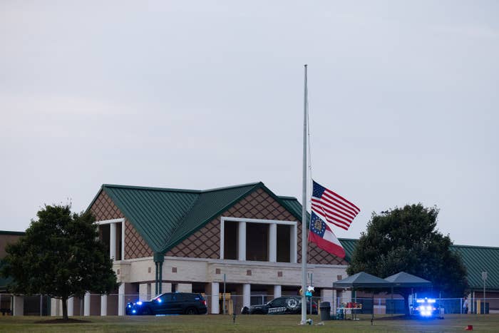 The image shows a building with the American flag at half-staff and police vehicles with flashing lights in front