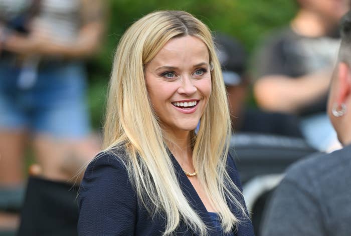 Reese Witherspoon, smiling and wearing a stylish blazer, interacts with someone off-camera at an outdoor event