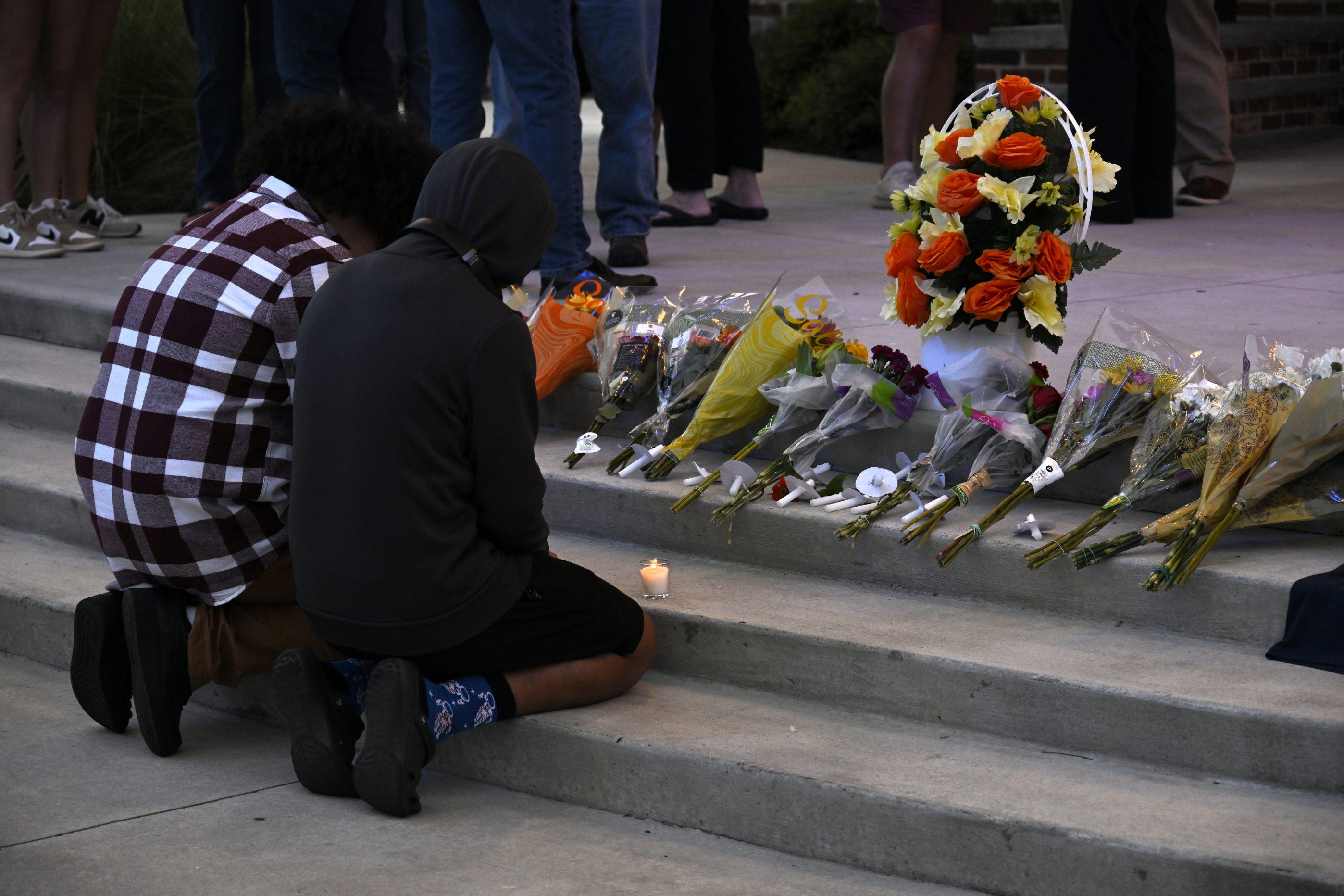 Mourners kneel by steps covered with flowers and candles during a vigil
