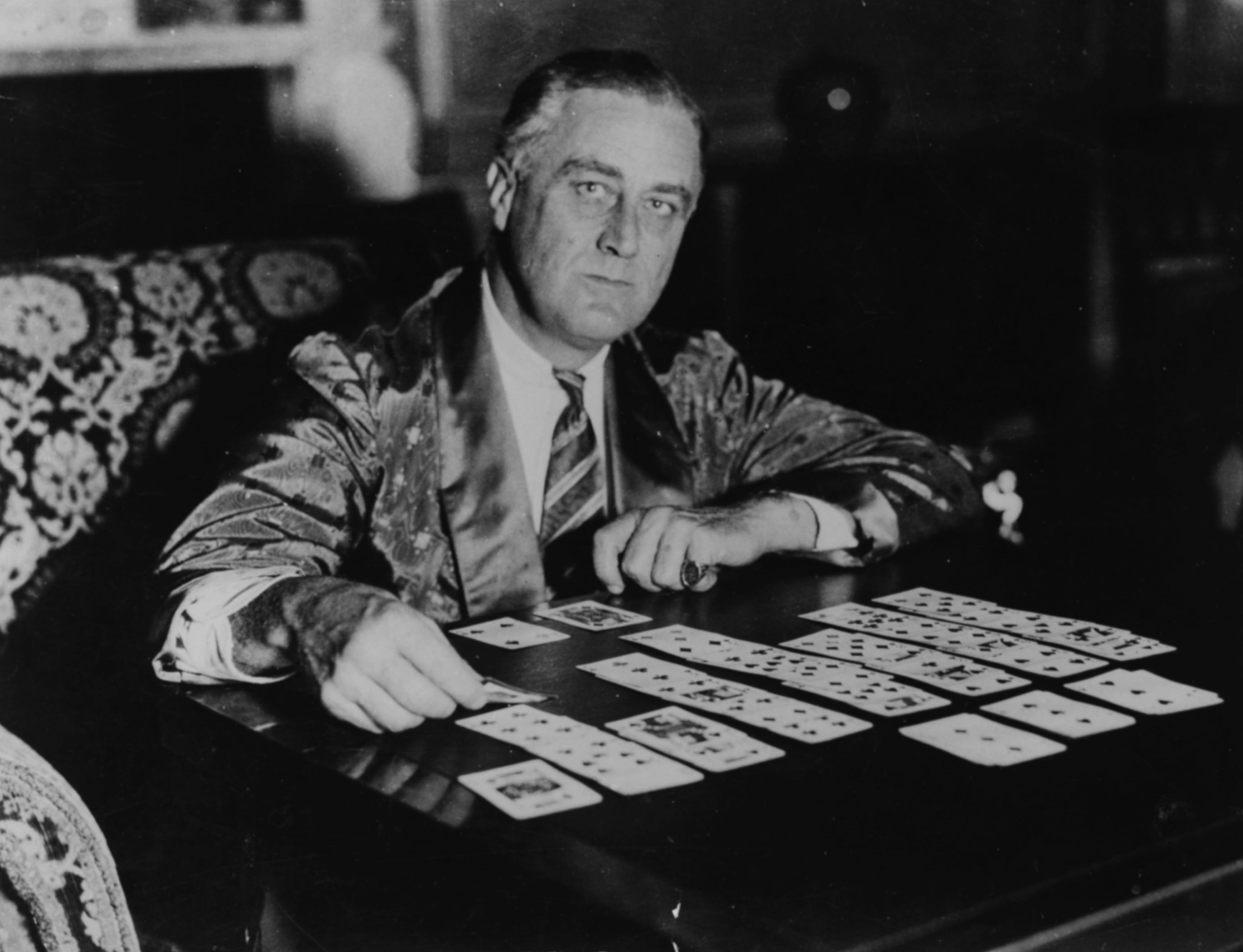 Franklin D. Roosevelt in a formal robe seated at a table playing solitaire with a focused expression
