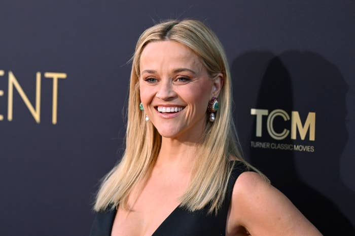 Reese Witherspoon smiles, wearing a sleeveless V-neck dress with drop earrings, at a Turner Classic Movies event