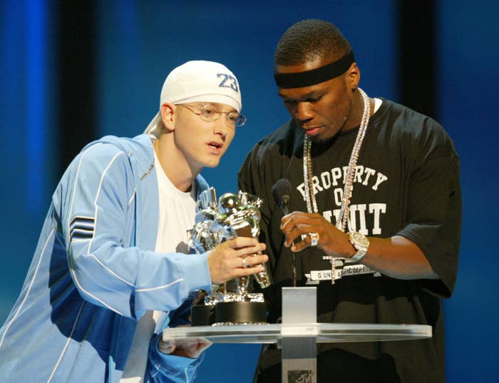 Eminem in a white hat and blue jacket and 50 Cent in a black T-shirt with &quot;Property of G-Unit&quot; on stage holding an MTV award