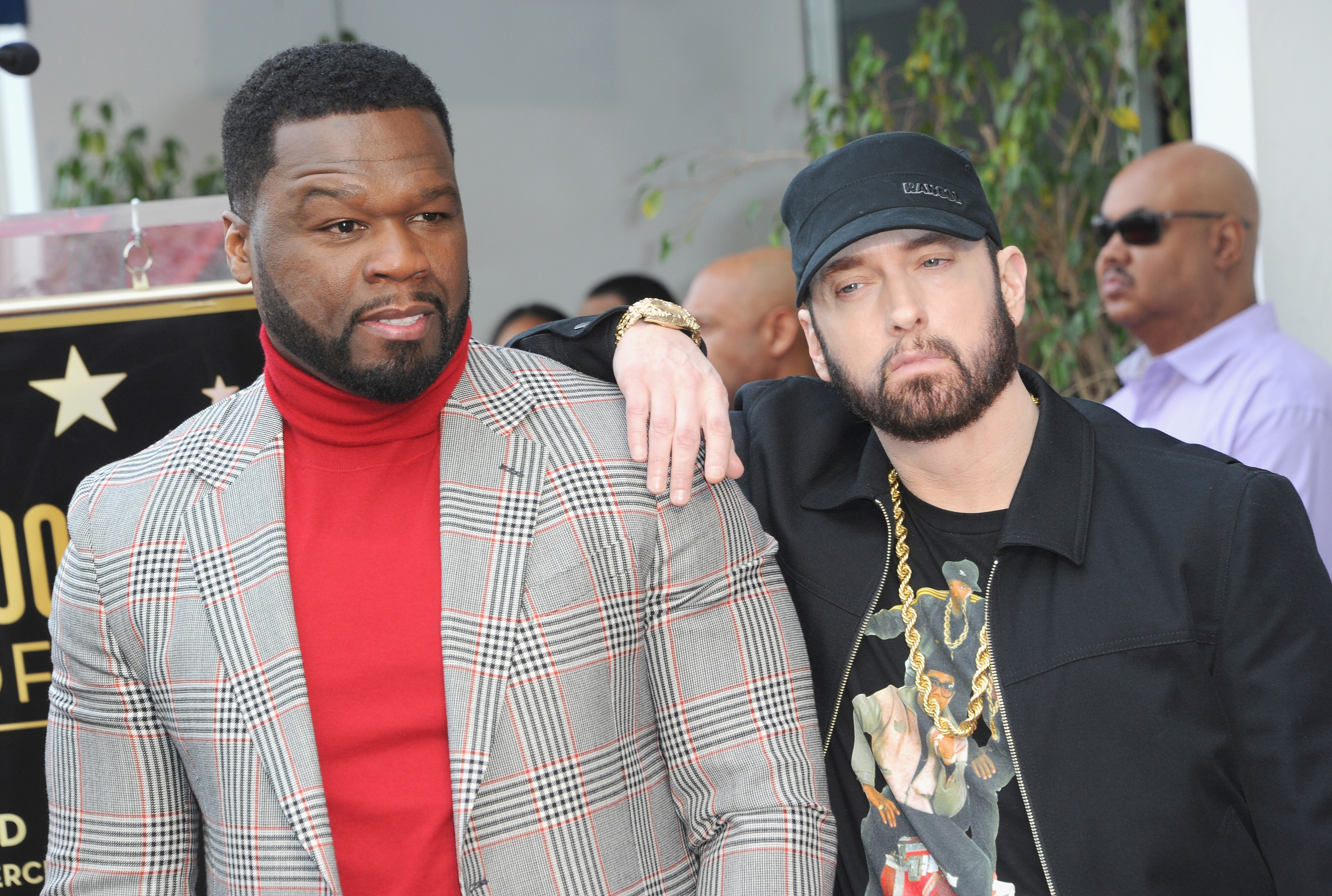 50 Cent in a plaid suit and Eminem in a casual outfit with a chain necklace pose together, with Eminem&#x27;s arm on 50 Cent&#x27;s shoulder